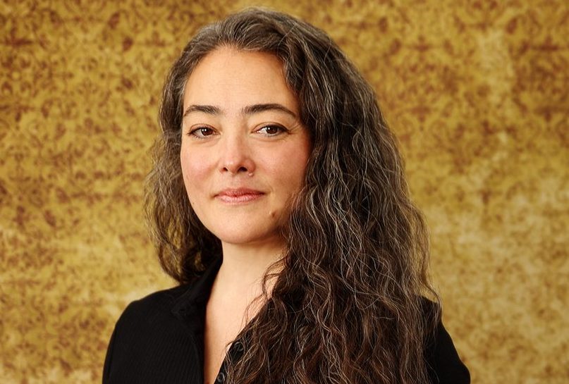 woman's face and shoulders, brown hair, black shirt, gold and brown background